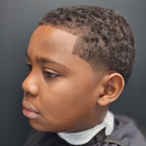 Boy in profile with a short, tight curly top, a low taper and a sharp line-up