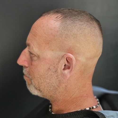 Man in profile with a high skin fade, a short top and trimmed grey stubble