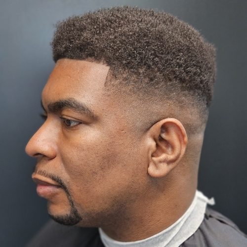 Man in profile with a curly top, a skin fade on the sides, a sharp line-up and a lined goatee